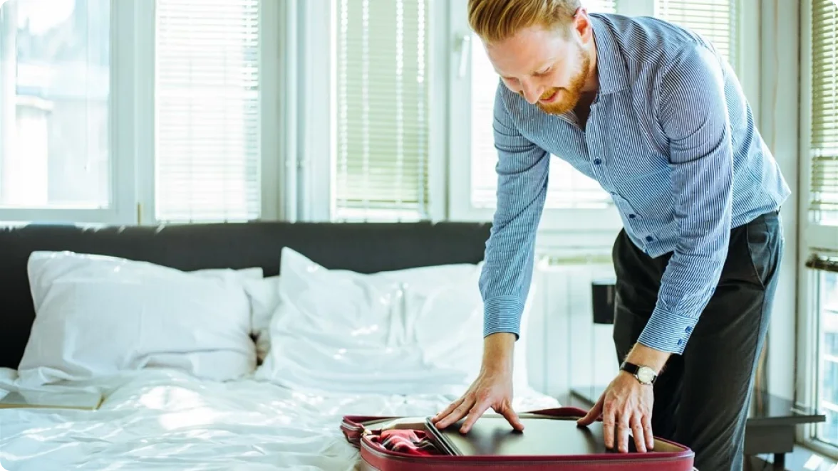 A man packing his suitcase on a bed.